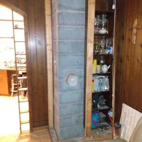 Bare chimney chase covered in grey sheeting inside a wood-panelled room